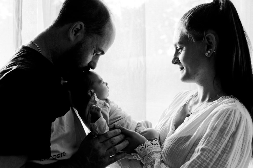 Un moment de pure tendresse entre jeunes parents et leur bébé lors d'une séance à domicile.
